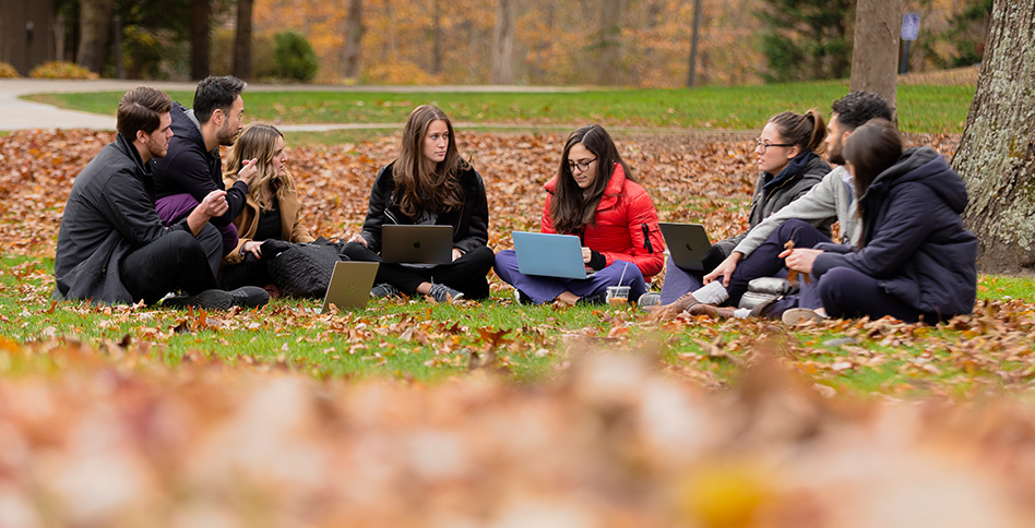 Students sitting in circle on ground outside using laptops