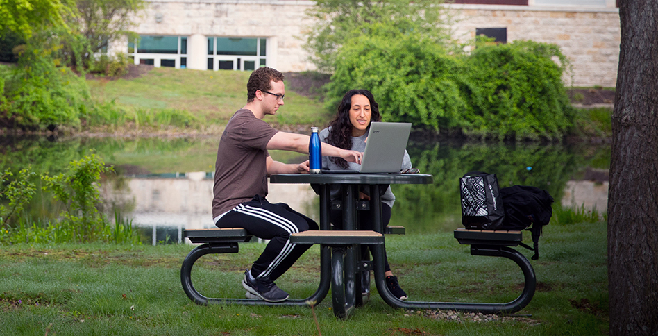 Two students at park table looking at laptop computer