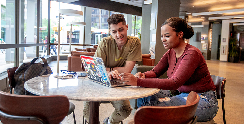 Two students seated at table and working on laptop 