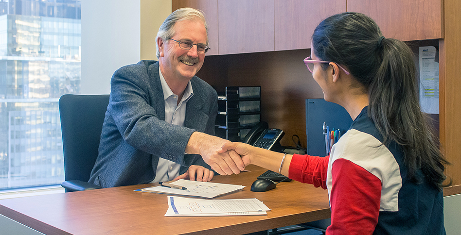 Student and administrator shaking hands across desk