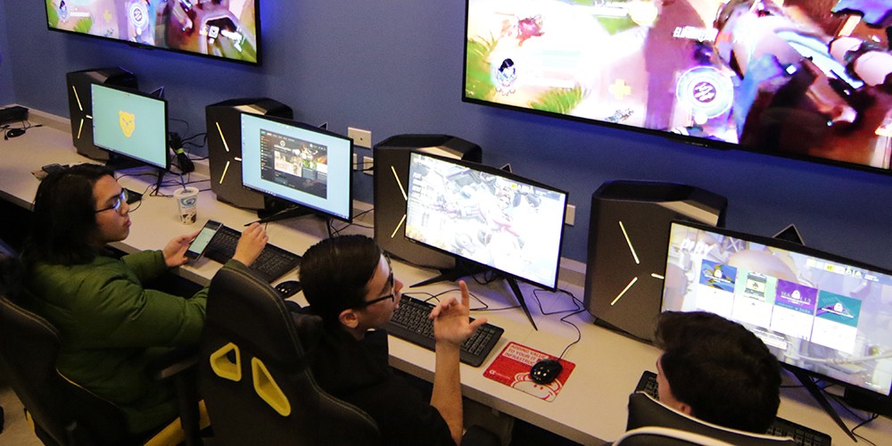 Students working on computer games with multiple screens.